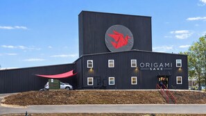 A modern building with a large red origami crane logo, a sign reading 'ORIGAMI SAKE,' and a small entrance with steps. - Lakefront Retreat w/Hot Tub, Fire Pit, Games! (Hot Springs)