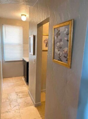 Enter a serene hallway leading to a cozy room with a window and a framed picture.