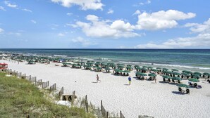 Una spiaggia con file di ombrelloni verdi e lettini, una recinzione in legno e l'oceano sullo sfondo.