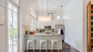 Una cucina moderna con mobili bianchi, una grande isola con sgabelli, un lampadario e vista attraverso una porta in vetro.