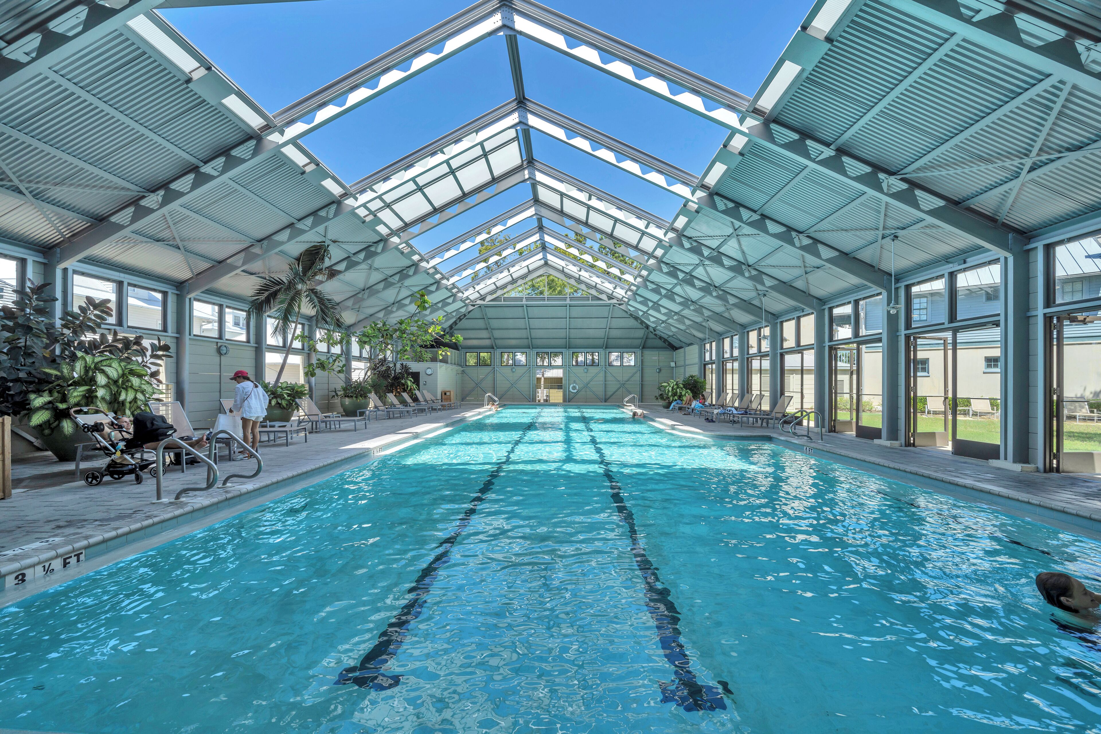 Une piscine intérieure dotée d’un toit en verre, de couloirs bien délimités et de chaises longues disposées le long des bords.