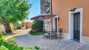 A patio with a table and chairs, a potted plant, and a building entrance. - Holiday apartment with pool near Porec (Poreč)
