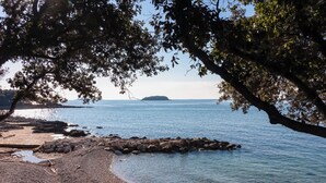 A beach with a rocky shoreline, calm water, and a distant island. - Holiday apartment with pool near Porec (Poreč)