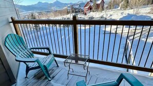 A wooden deck with two teal chairs and a small table, overlooking a snowy landscape with houses and a mountain in the distance. - 2 BR Mountain Condo w/ views, near amazing skiing (Silverthorne)