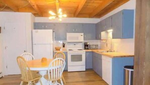 A compact kitchen with wooden cabinets, a white refrigerator, a microwave, and a sink. There is a dining table with two chairs and a trash bin. - 2 BR Mountain Condo w/ views, near amazing skiing (Silverthorne)
