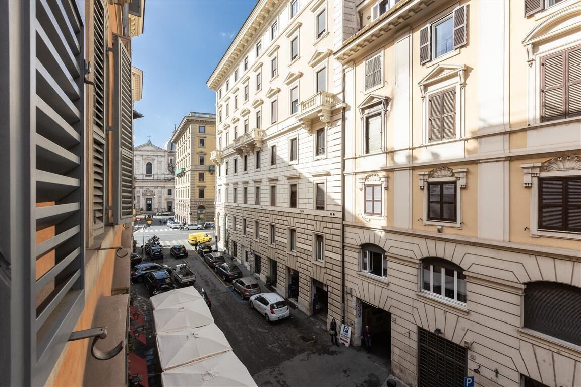 A narrow street lined with multi-story buildings, parked cars, and outdoor seating areas.