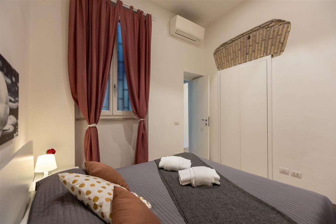 Ein Schlafzimmer mit Bett, Kissen, einem Fenster mit Vorhängen, einer Klimaanlage, einem Kleiderschrank und einer Lampe.