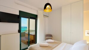 Ett hotellrum med en säng, en stol, utsikt över havet och en skjutdörr i glas som leder ut till en balkong.
