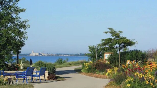 A pathway leading to a seating area with chairs, surrounded by colorful flowers and trees, overlooking a body of water with distant buildings. - {{{ Mid-Century Modern }}} Newly renovated 3 BR (Two Rivers)