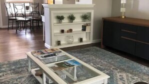 A living room with a glass coffee table, a patterned rug, a white shelving unit with plants, and a dark cabinet. - {{{ Mid-Century Modern }}} Newly renovated 3 BR (Two Rivers)