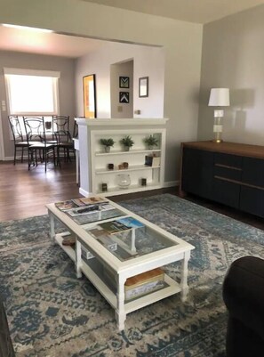 Cozy living space with a central coffee table and dining area, featuring a shelving unit and cabinet.