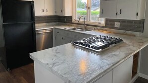 A modern kitchen with white cabinets, a black refrigerator, a stainless steel sink, and a gas stove. - {{{ Mid-Century Modern }}} Newly renovated 3 BR (Two Rivers)