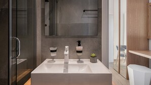 Ein modernes Badezimmer mit einem großen Spiegel, einem weißen Waschbecken und einer Duschkabine.