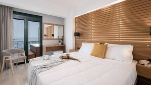 Ein modernes Hotelzimmer mit einem großen Bett, einem Schreibtisch, einem Sessel und einem Balkon mit Meerblick.