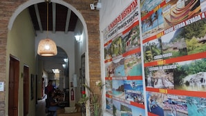 Un pasillo con un cartel que anuncia varios tours, una lámpara colgante y una persona trabajando en un escritorio.