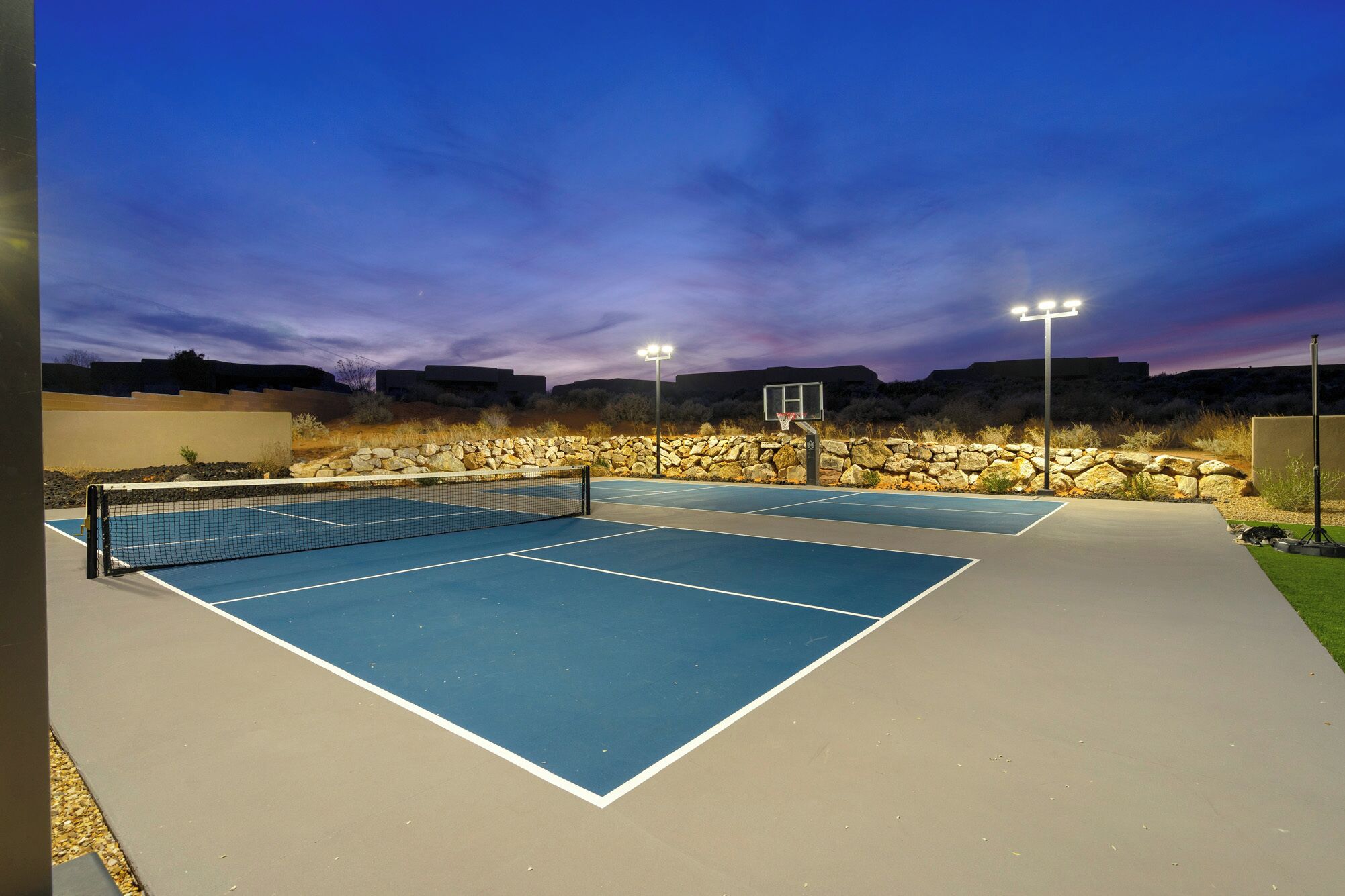 An outdoor tennis court with a stone wall and lighting.