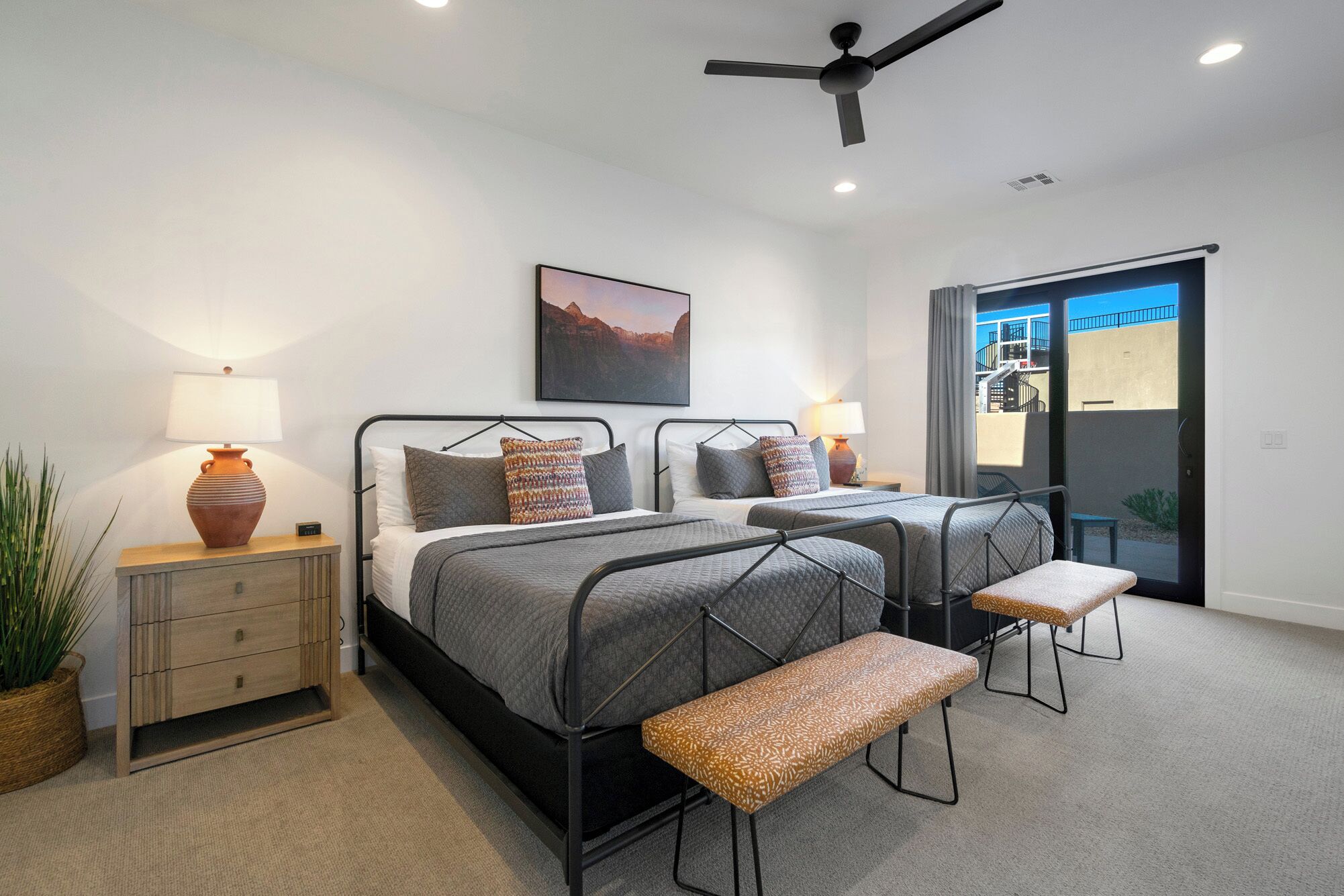 A modern bedroom with two beds, a ceiling fan, and a large window with a view of a building.