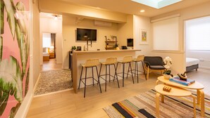 A modern living room with a kitchen area, bar stools, and a television. - Charming 4-Bedroom Retreat in Heart of Condado (San Juan)