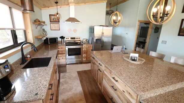 Una cocina con encimeras de granito, armarios de madera, electrodomésticos de acero inoxidable e iluminación colgante.