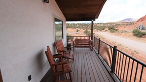 Una terraza de madera con mobiliario exterior, vista a un paisaje desértico y una montaña al fondo.