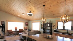 Amplia sala de estar con techo de madera, una isla grande con taburetes de bar, un conjunto de sofás y una cocina con pileta y encimera.