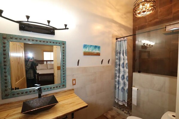 A bathroom with a wooden vanity, a large mirror with a decorative frame, a shower with a glass door, and a ceiling light fixture. - Peace, Privacy, Serenity and Panoramic Views from all windows.
One of a Kind (Torrey)