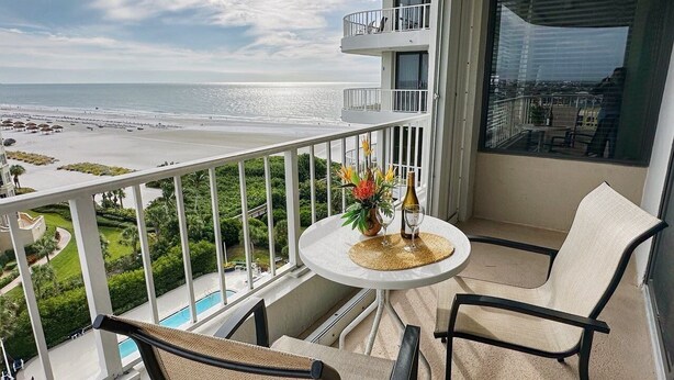 A balcony with a table, chairs, and a view of the beach and ocean. - Beachfront Condo available on a Monthly Basis Only (Marco Island)