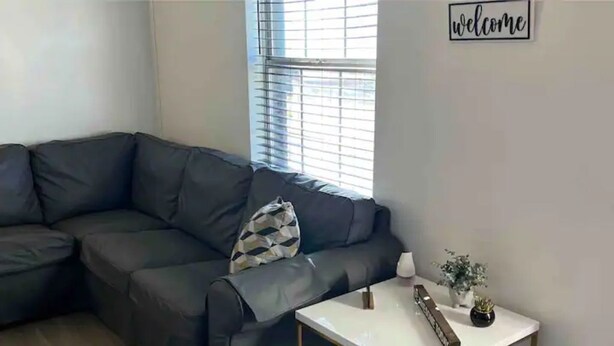 Una sala de estar moderna con un sofá de cuero oscuro, una mesa de centro blanca y un cartel con la palabra 'welcome'.