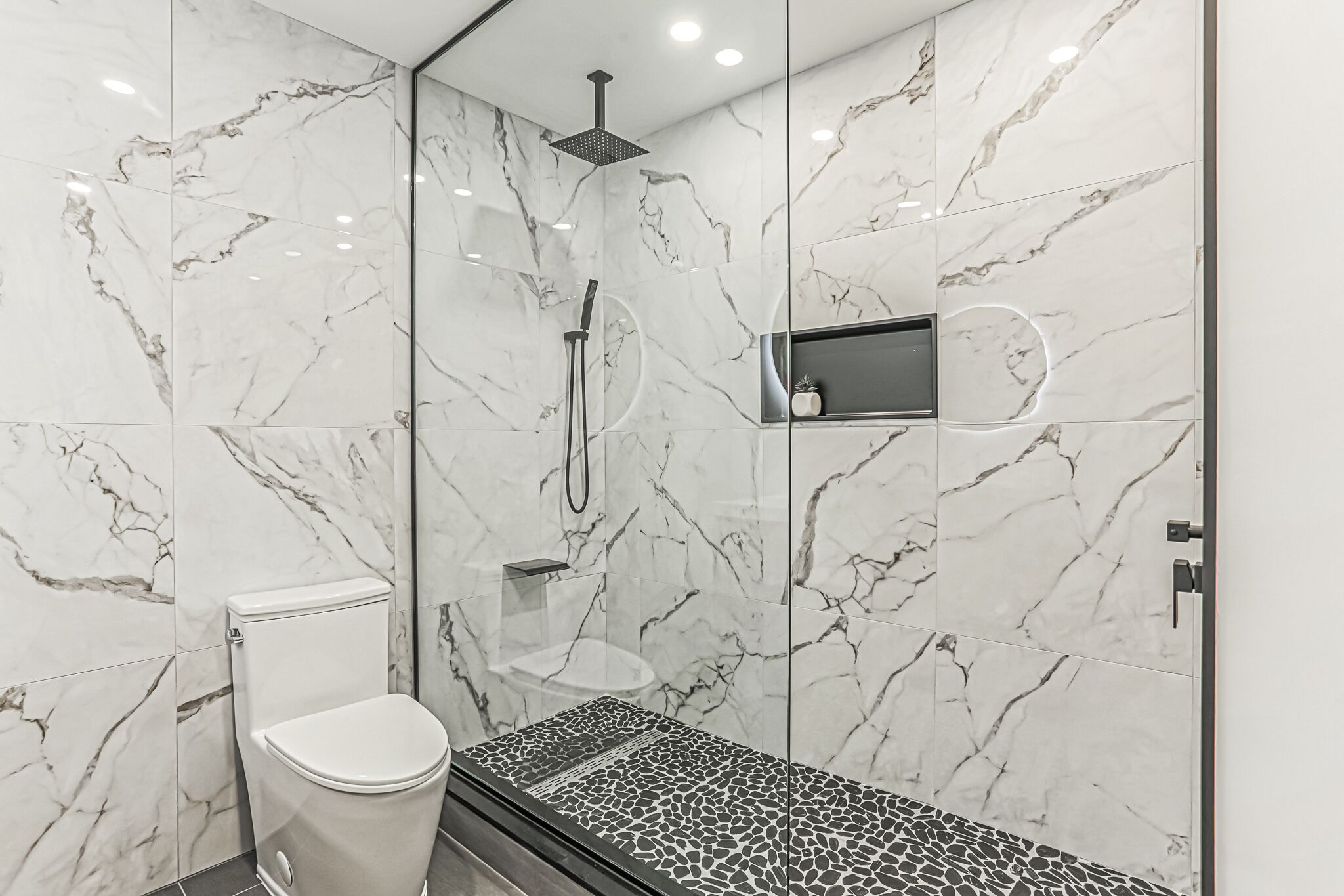 Ein modernes Badezimmer mit Marmorwänden, einer gläsernen Duschkabine, einer Toilette und einer Sitzbank.