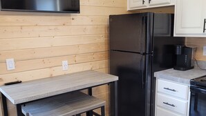Eine kleine Küche mit Holzwänden, einem schwarzen Kühlschrank, weißen Schränken, einer eingebauten Mikrowelle und einem Tisch mit einer Bank.