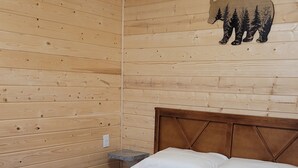 Ein Zimmer einer Holzhütte mit einem Bett, einem Nachttisch und einer Wanddekoration mit Bär und Bäumen.