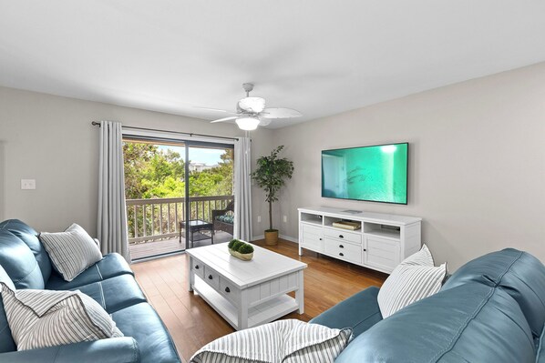 A modern living room with a blue sofa, white coffee table, and a TV on the wall.