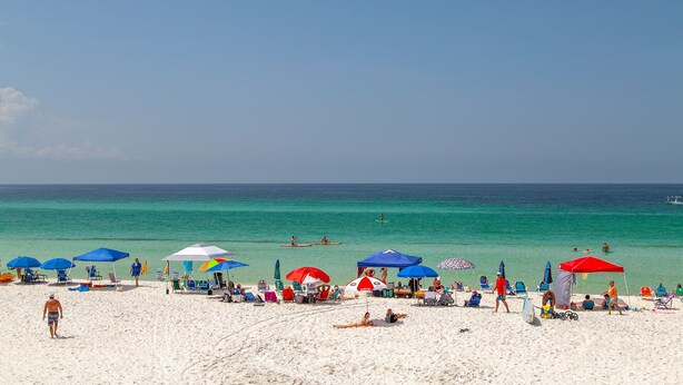 Una playa con arena blanca, agua turquesa cristalina y varias sombrillas que dan sombra.