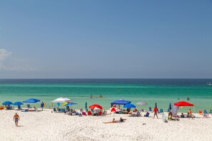 A beach with white sand, clear turquoise water, and several umbrellas providing shade.
