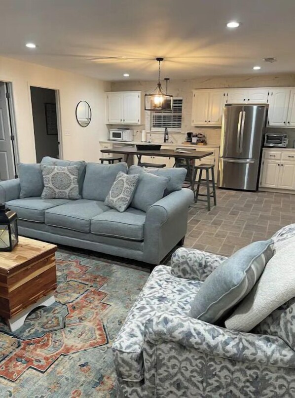 Relax in this stylish living room with a sofa, coffee table, and rug, adjacent to a well-equipped kitchen area.