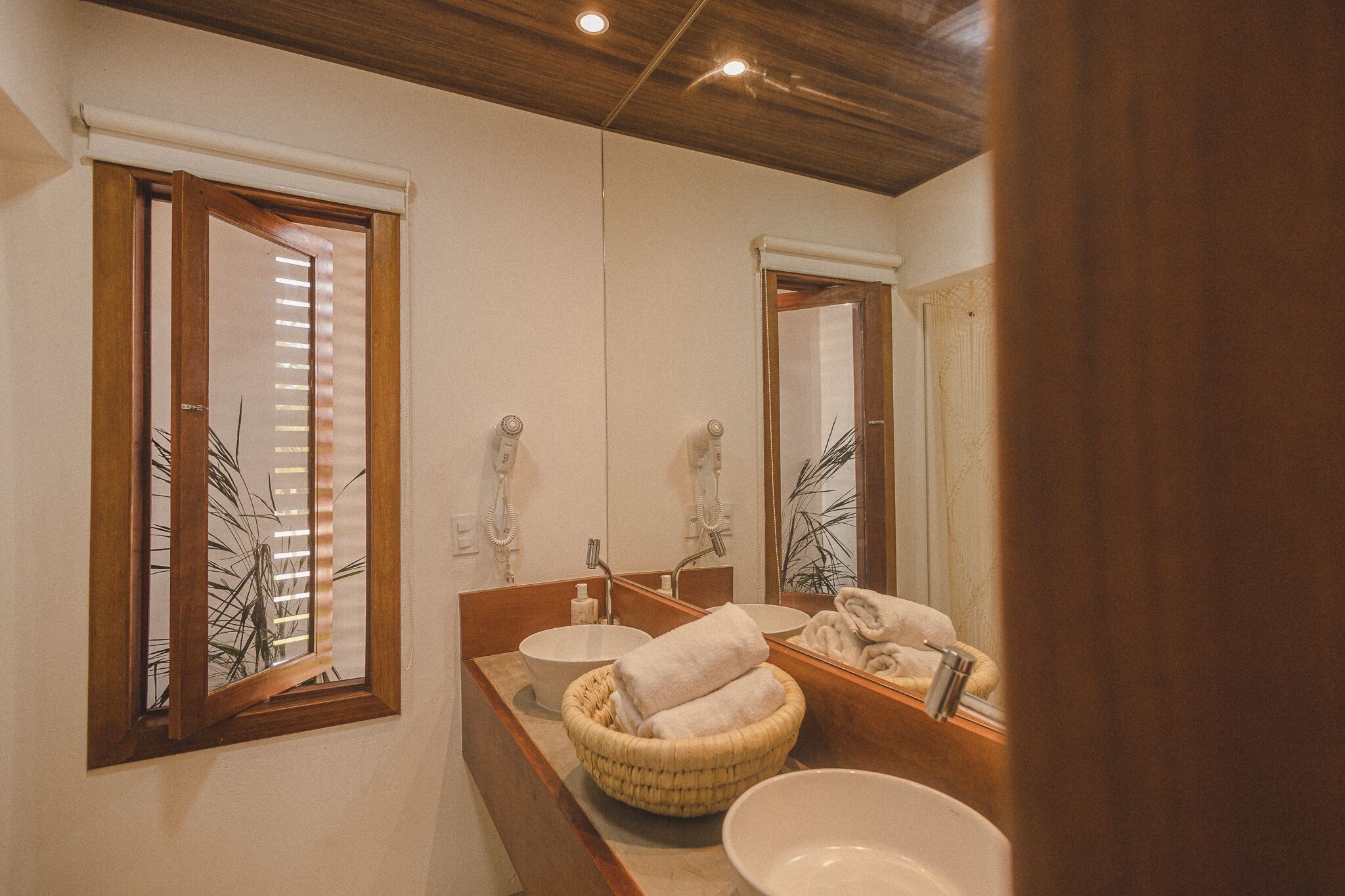 A bathroom with a wooden vanity, two sinks, a large mirror, and a window with blinds.