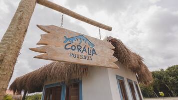 Uma placa de madeira com o texto 'Coráia Pousada' pendurada sobre um edifício com telhado de palha.