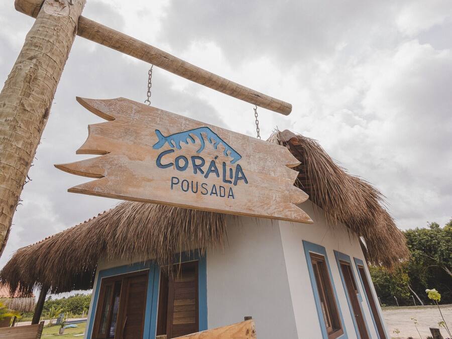 Uma placa de madeira com o texto 'Coráia Pousada' pendurada sobre um edifício com telhado de palha.