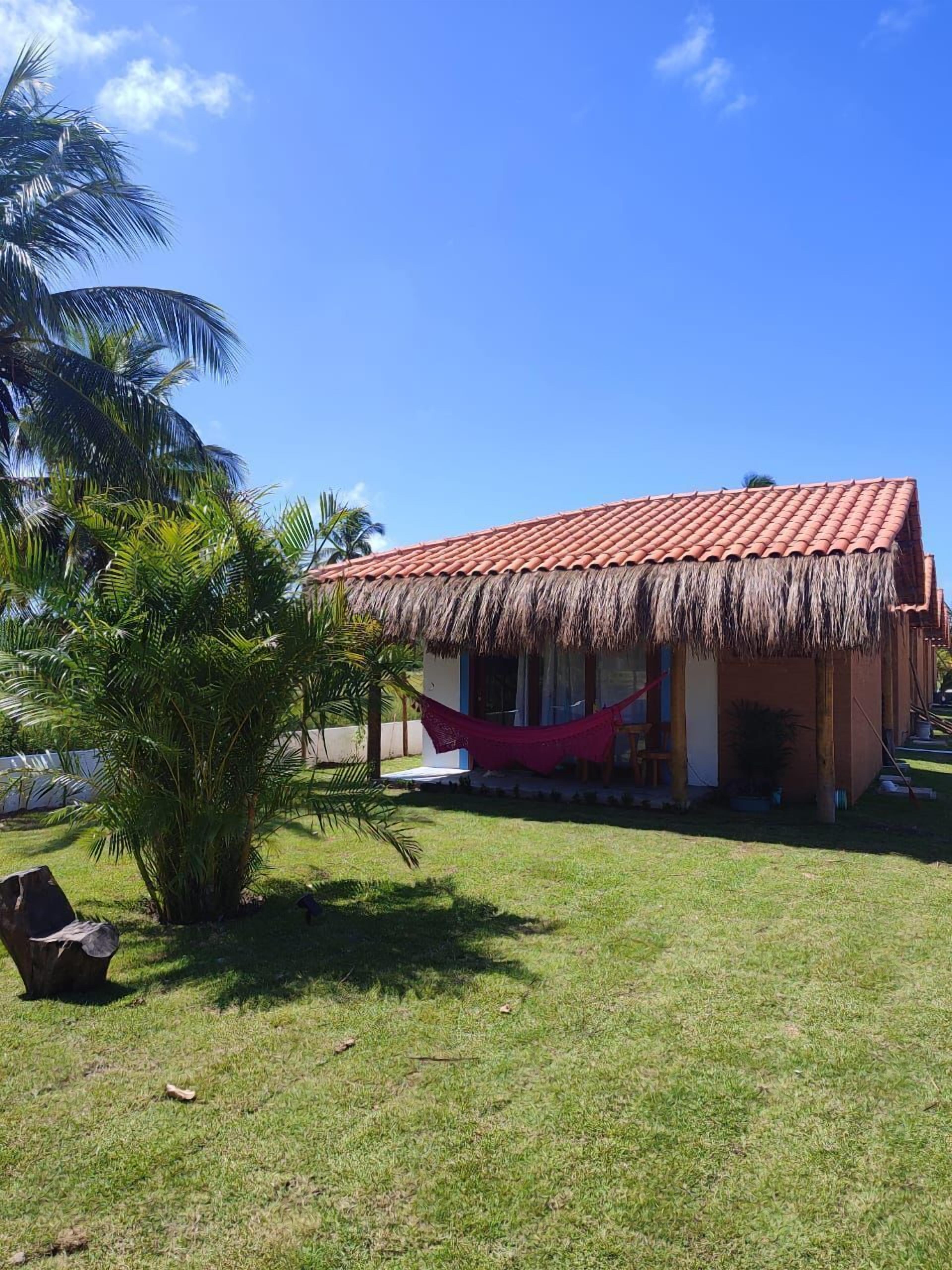 A house with a red tiled roof and a thatched roof over the porch.