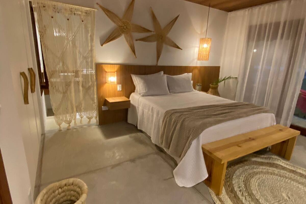 A bedroom with a wooden ceiling, a bed with white bedding, a star decoration, a bedside lamp, and a woven basket.