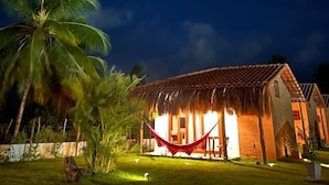 A thatched-roof building with a hammock in front, surrounded by palm trees and a clear night sky. - Pousada Corália (São Miguel dos Milagres)