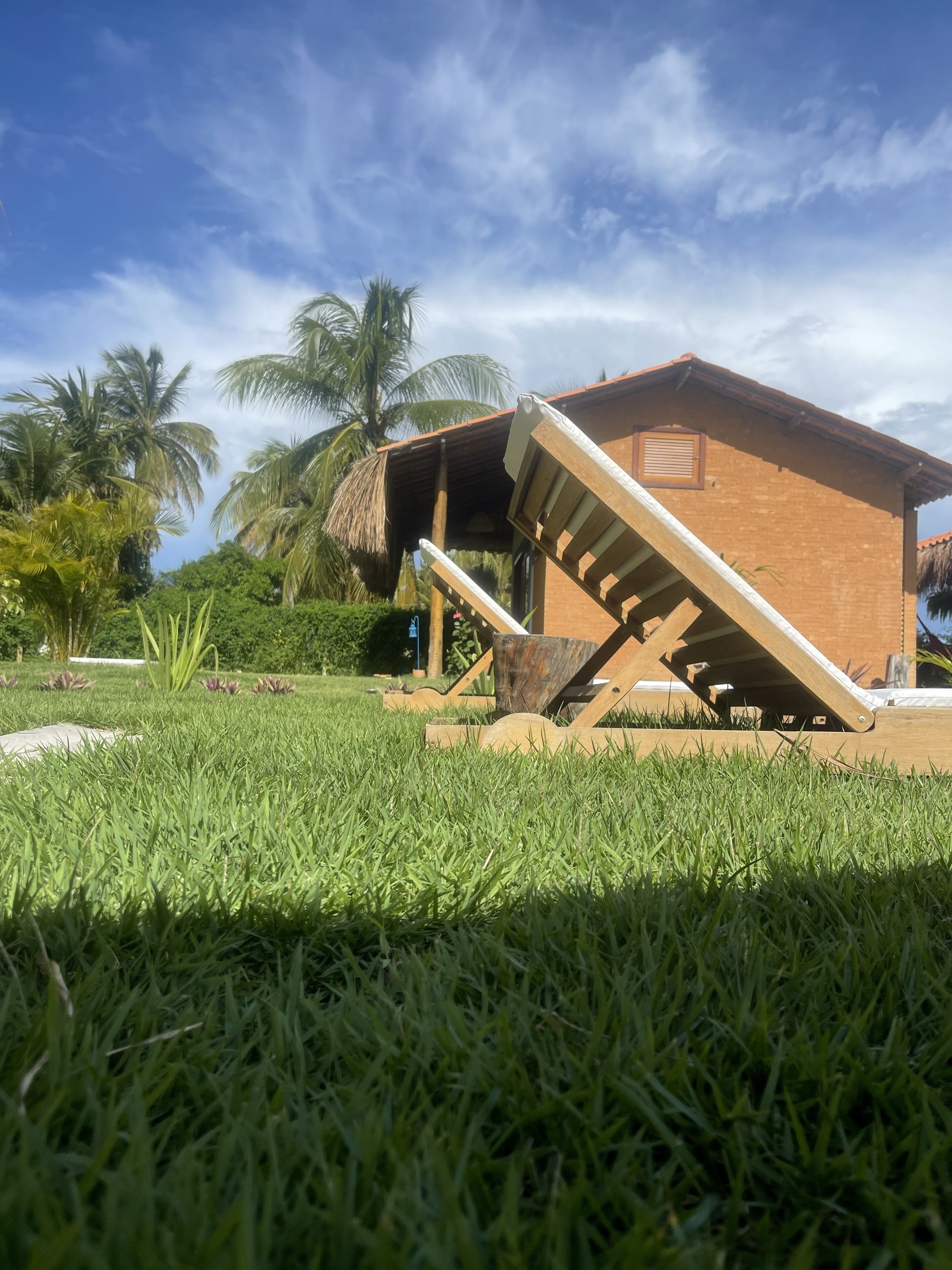 Una casa con una escalera de madera que conduce a un porche cubierto, rodeada de abundante césped verde y palmeras.