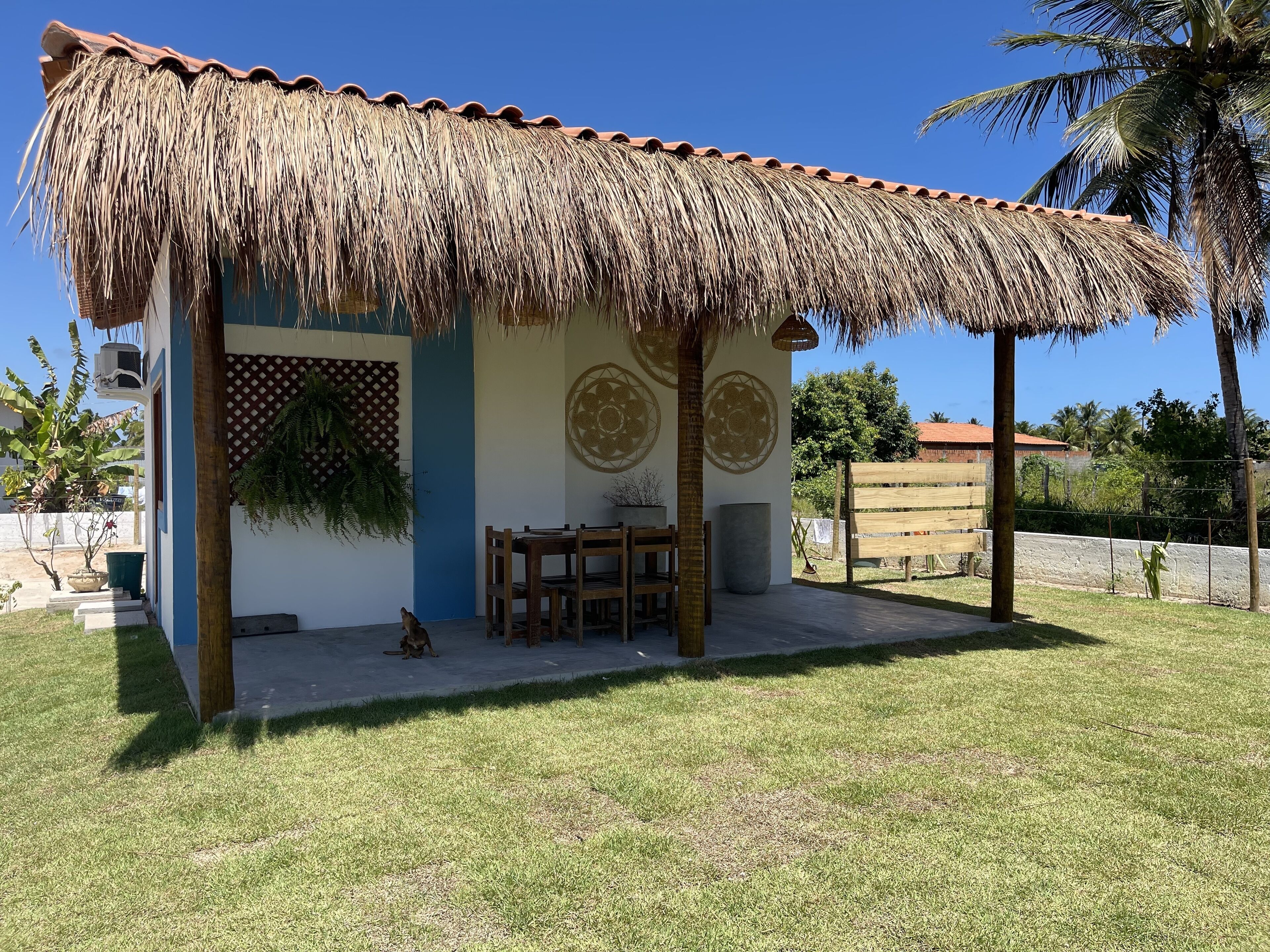 Un pequeño edificio de una sola planta con techo de paja, un comedor con muebles de madera y paneles decorativos en las paredes.