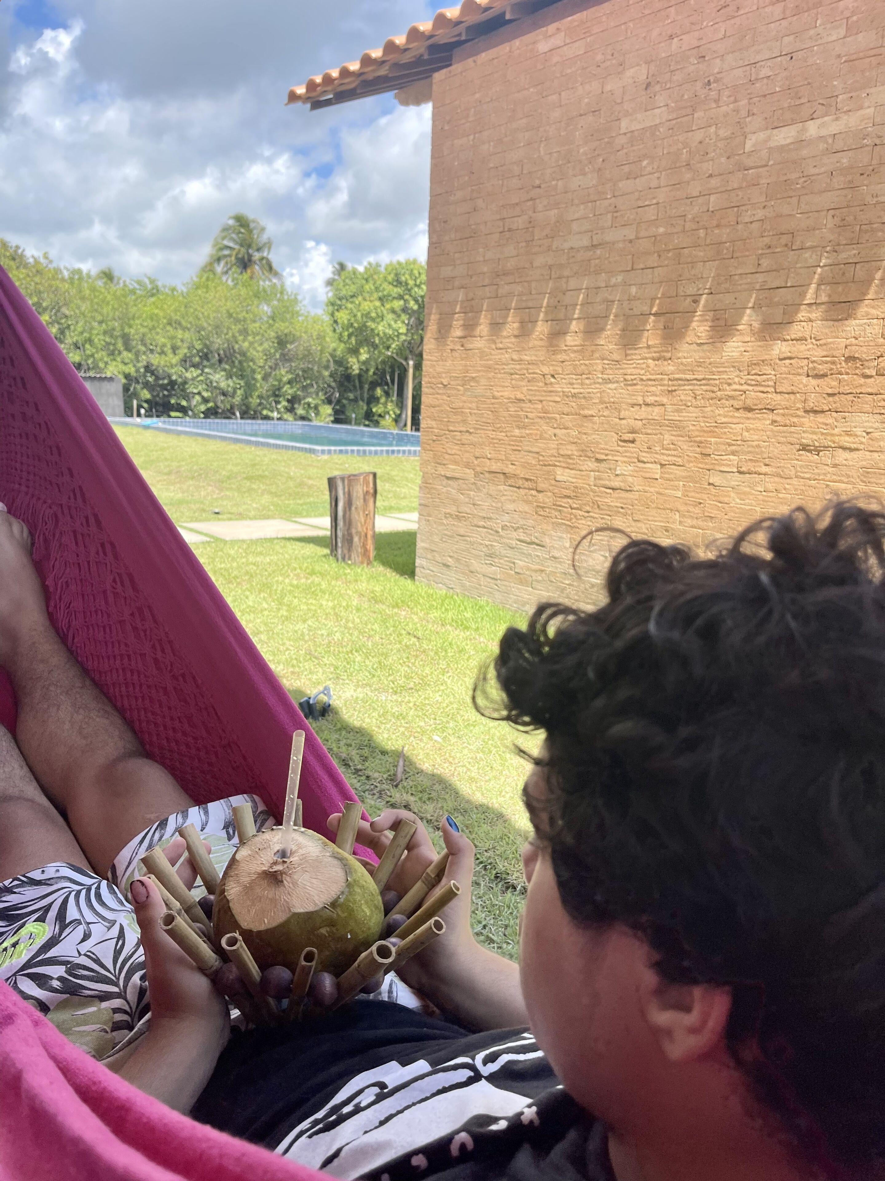 Une personne allongée dans un hamac rose, à l’extérieur, tenant une noix de coco.