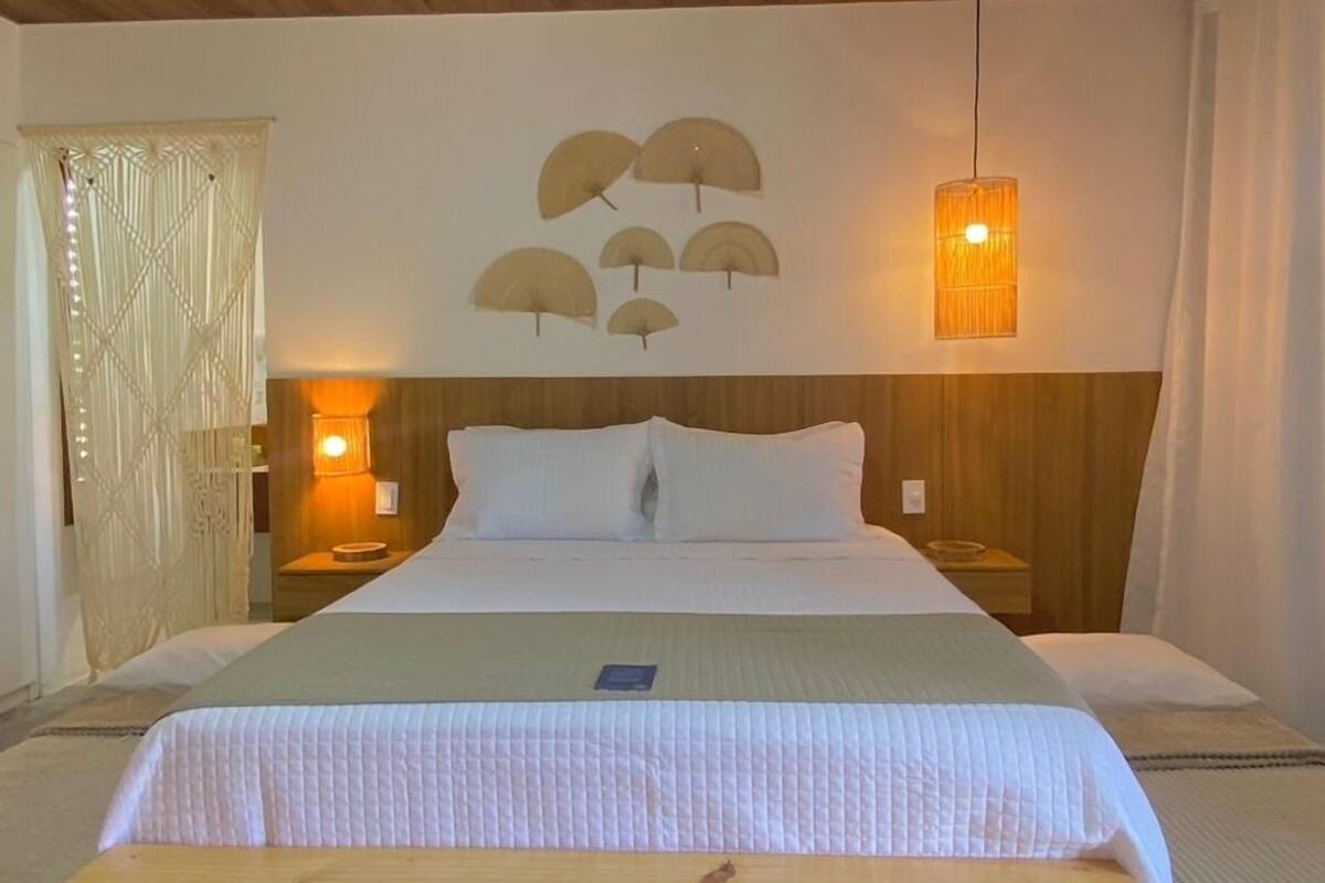 A bedroom with a wooden ceiling, a bed with white bedding, a wooden bench, a woven rug, and wall-mounted lamps.