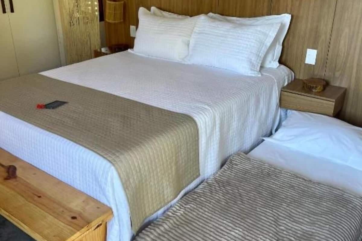 A neatly made bed with a wooden headboard, a bedside table with a lamp, and a bench at the foot of the bed.