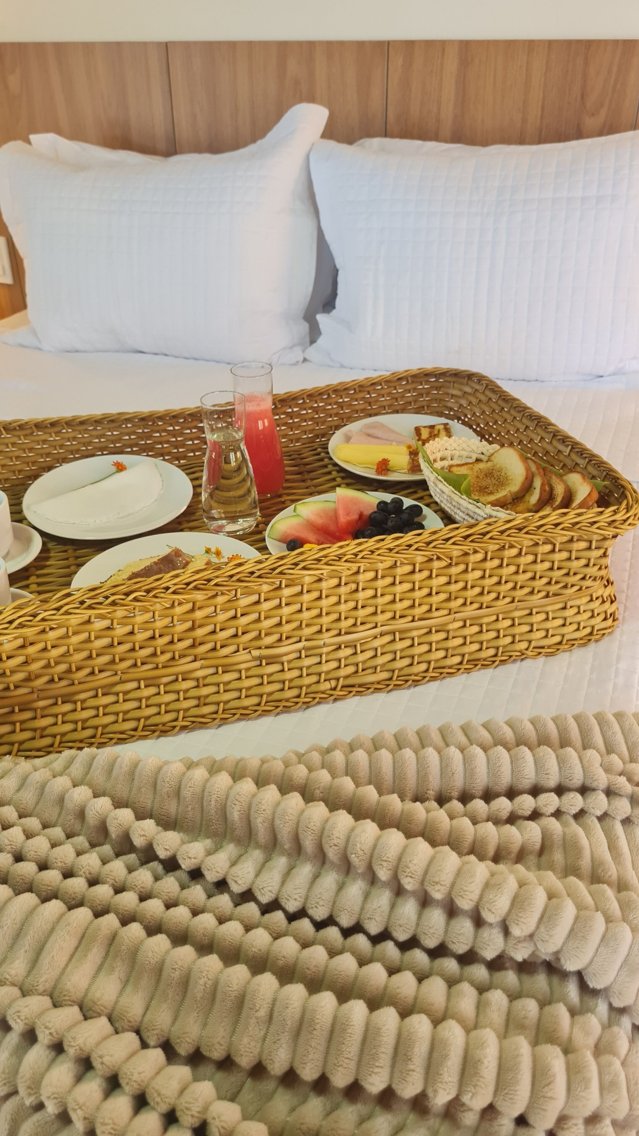 A neatly made bed with a breakfast tray containing fruits, bread, and a glass of juice.