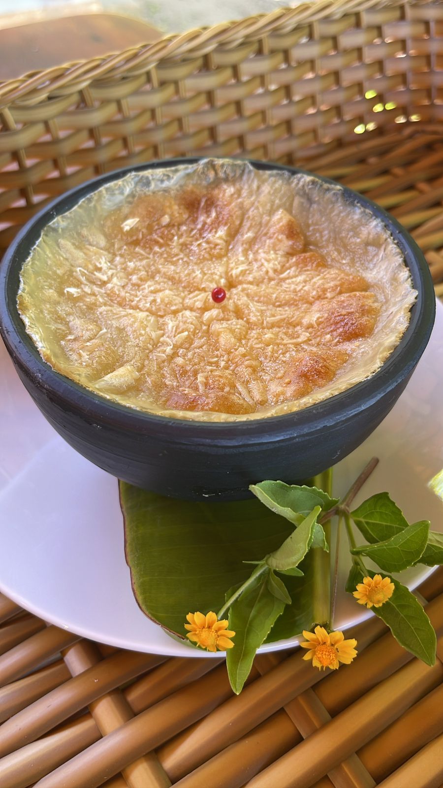 A bowl of food on a plate with a woven mat underneath.