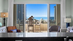 A balcony with a view of the ocean and a building. There are two chairs and a table.