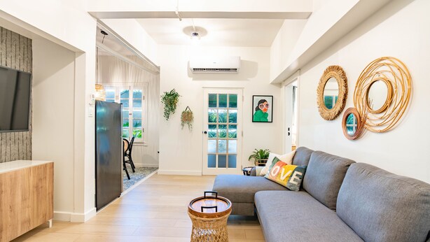 A modern living room with a grey sofa, a wicker coffee table, and decorative mirrors on the wall. - Condado Beach Chic - Walk everywhere (San Juan)